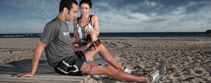 Pareja empleando electroestimulador en la playa