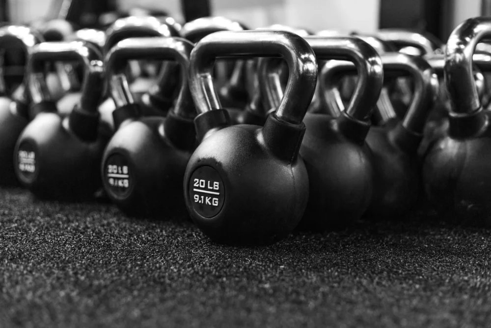 Persona levantando una kettlebell del suelo con la espalda recta en un gimnasio