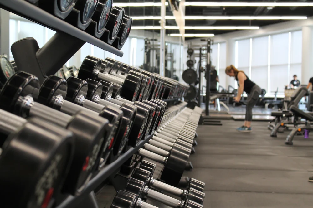 Zona de gimnasio con cintas de correr al fondo y mancuernas en primer plano