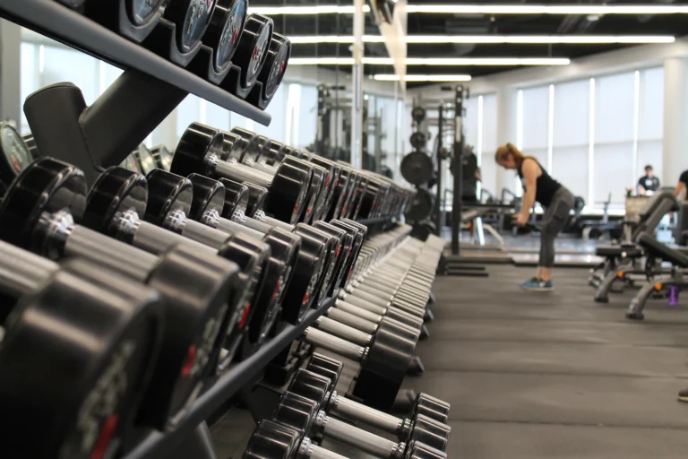 Zona de gimnasio con cintas de correr al fondo y mancuernas en primer plano